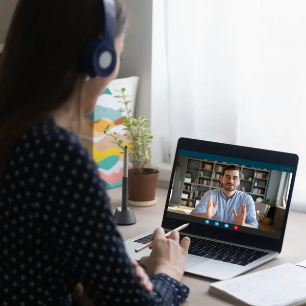 A learner wearing headphones studies with a teacher on a laptop.